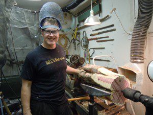 A man wearing goggles and a helmet stands in front of a machine.