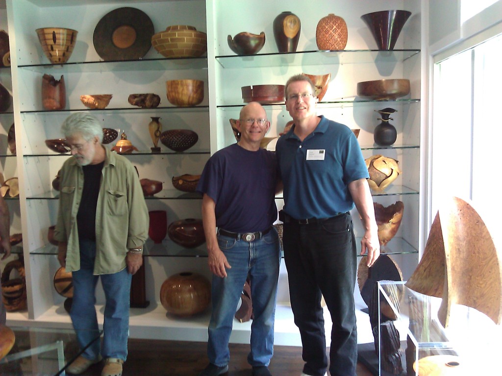 Three men standing in front of a wall full of bowls.